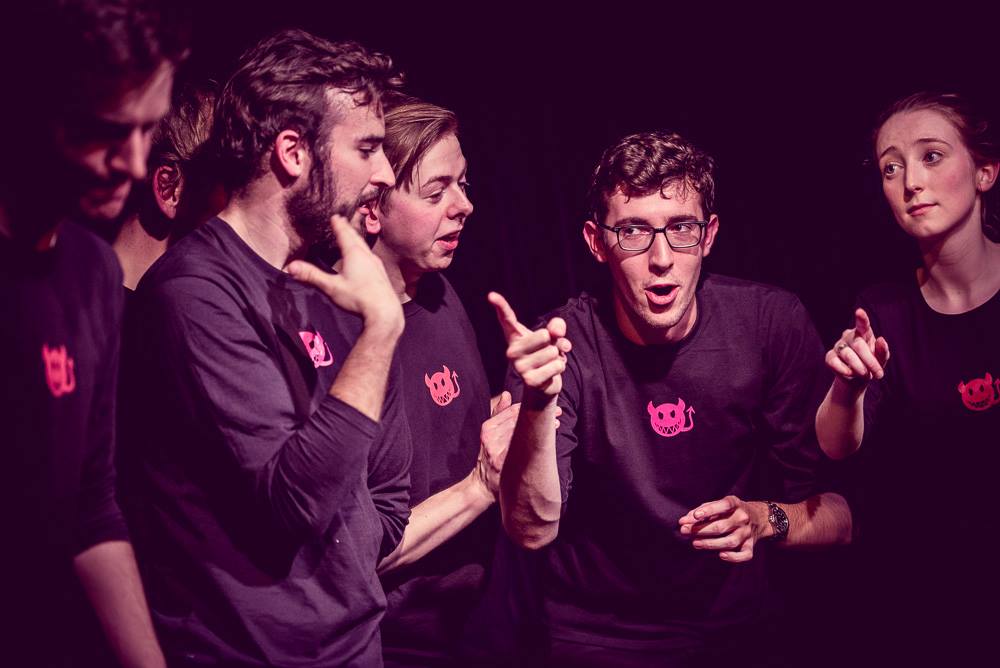 A group of the 'Oxford Imps' improv comedy troupe performing together on stage