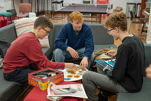 Three students sitting in a common room, playing a board game