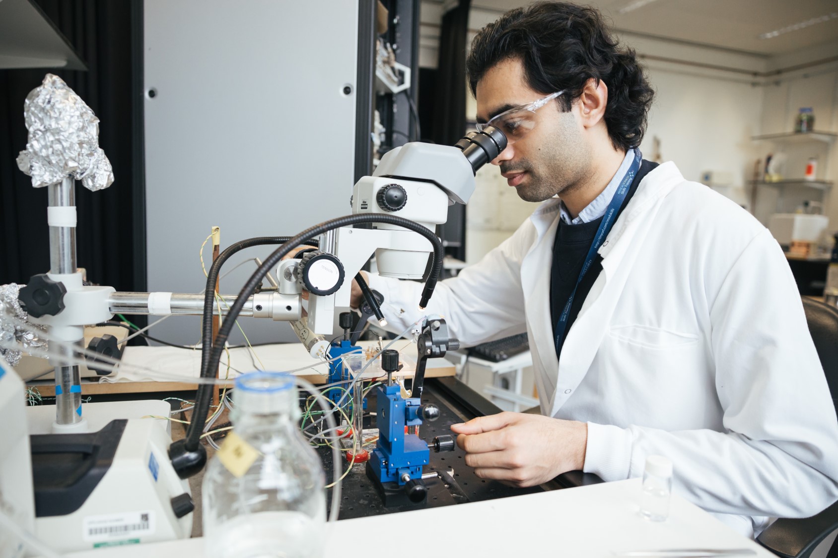 A student in a lab coat looking down a microscope in a lab