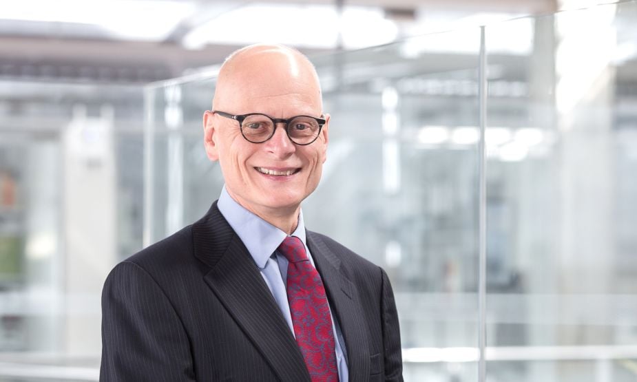 A bald white man wearing glasses, a smart jacket and a tie.