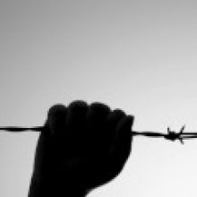 Hand in silhouette grasping barbed wire.