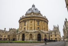 Landscape photo of the Radcliffe Camera and surrounding buildings with a cyclist in the foreground