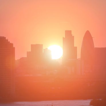 Silhouette of the city of London skyline, illuminated with an orange glow by the setting sun behind.