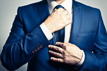 Businessman in blue suit tying the necktie: a ritual of sorts