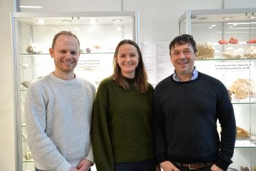 Dr Simon Stephenson (white man, brown hair), Associate Professor Claire Nichols (white lade, long brown hair), Associate Professor Jon Wade (white man, dark hair). They stand in front of two cabinets containing rocks and shells.