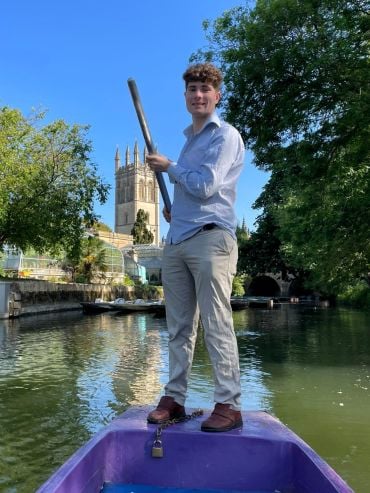 Conor punting on a river in Oxford with Magdalen College tower in the background.
