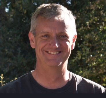 A portrait photograph of Patrick Irwin, a middle-aged man with greyish brown hair.