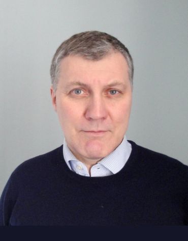 Photo of Professor Michael Keith, an older middle-aged white man with short grey hair wearing a shirt and dark blue jumper.