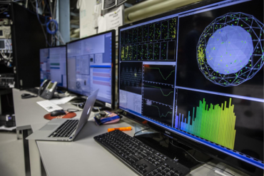 A bank of three computer screens showing graphs, data and simulations.