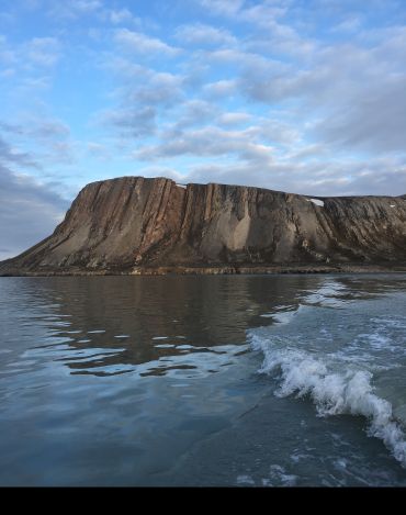 A cliff face overlooking a beach with waves in the foreground. Credit: Ross Anderson / University of Oxford. 