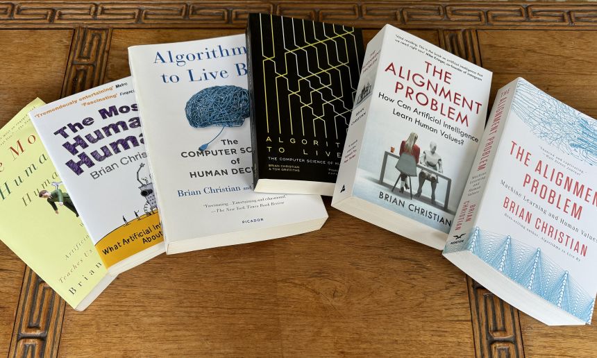 Five paperback books spread across a table. The titles are The Most Human Human’, ‘Algorithms to Live By’, and ‘The Alignment Problem.’