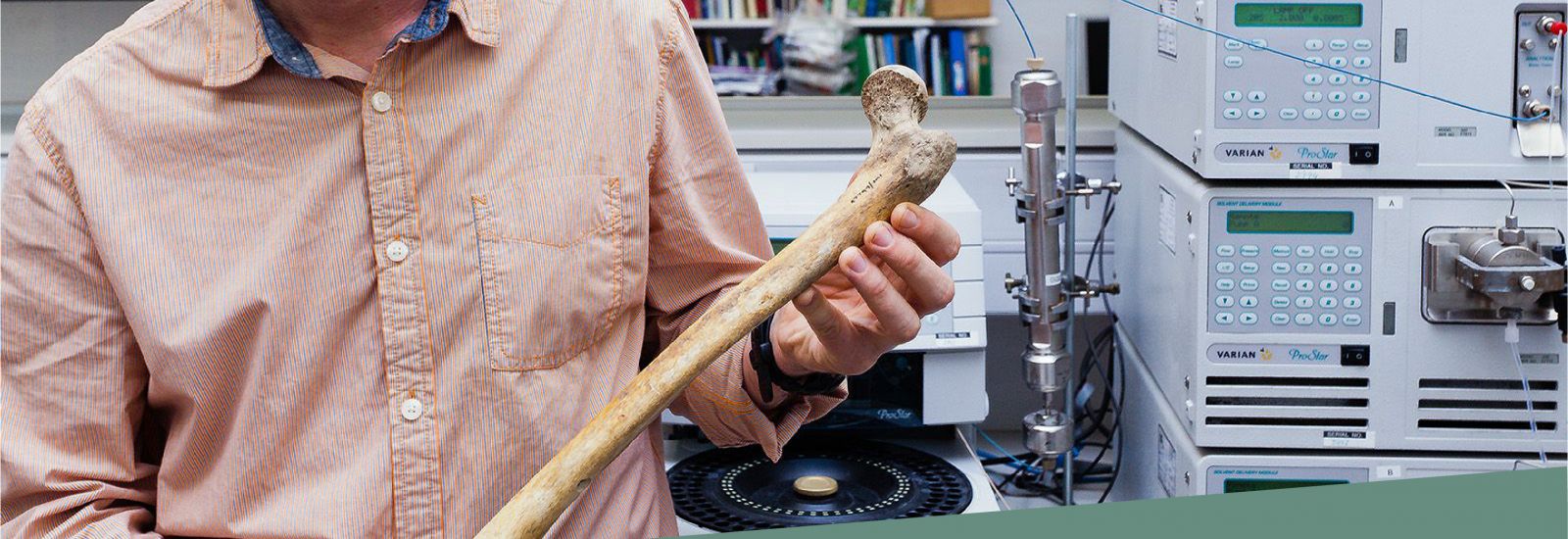 A tutor holding a bone in front of machines in an Archaeology lab