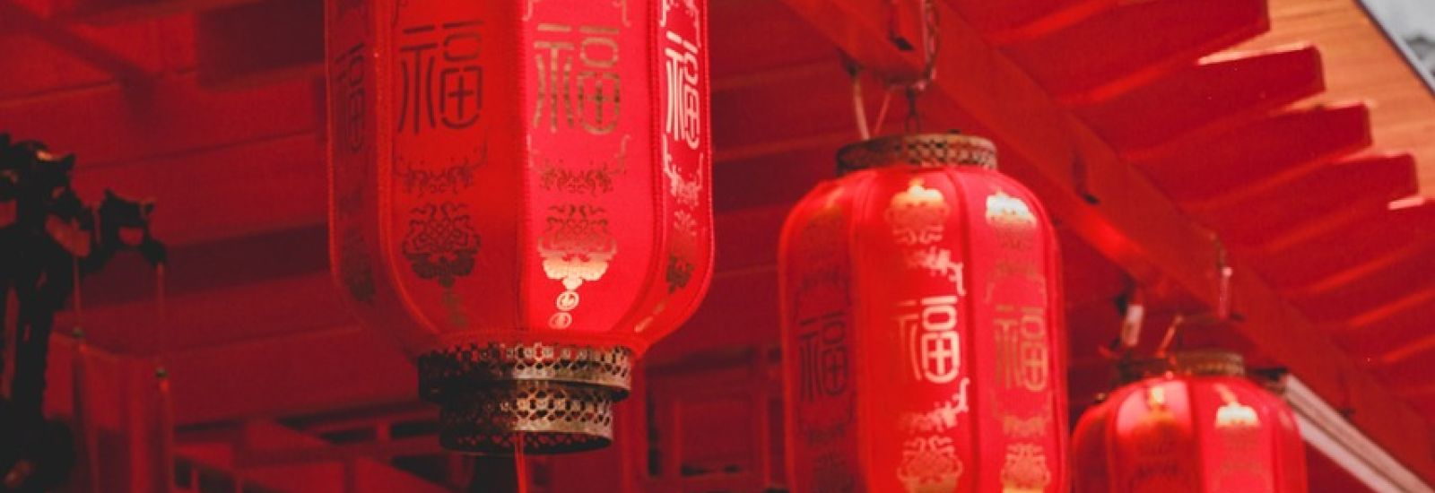 A red, Chinese building is decorated with red hanging lanterns adorned in Chinese characters