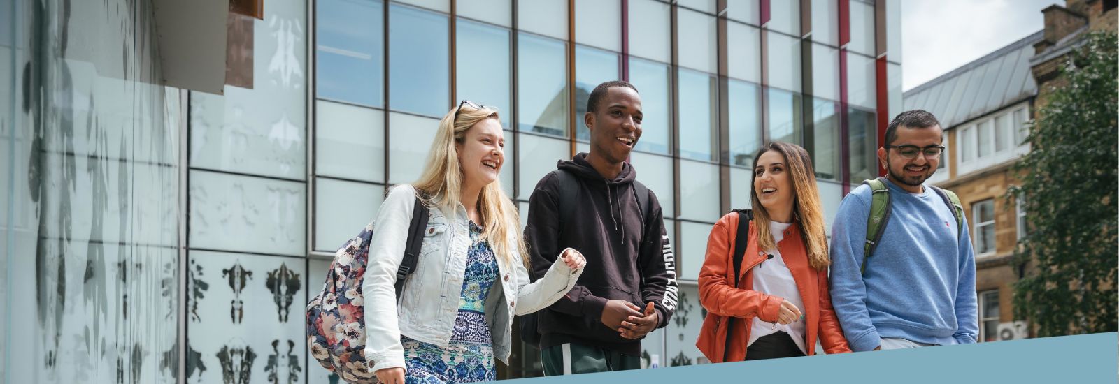Four students talking while walking in front of the glass wall of an Oxford building 