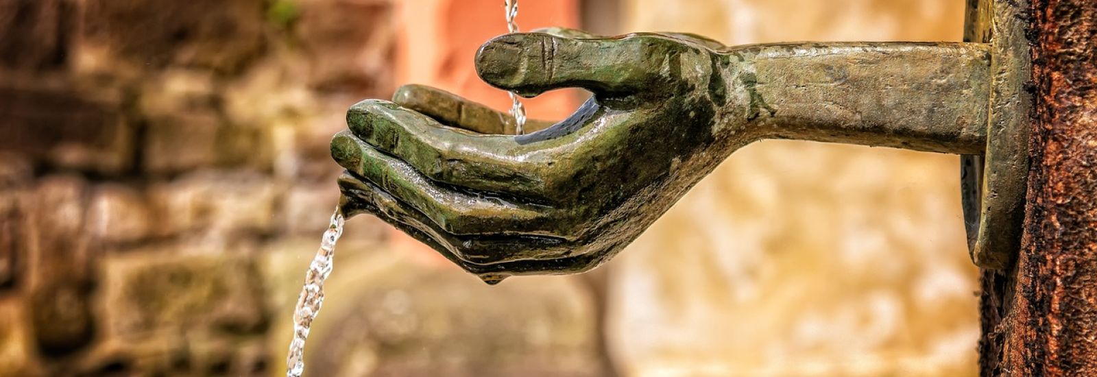An outdoor fountain, shaped like hands, cupping to catch the water that is falling.
