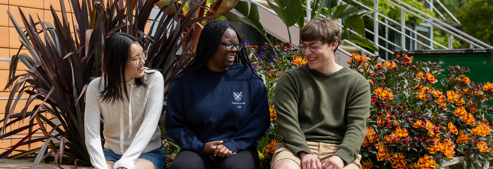Three students sitting on a bench laughing together Three students sitting on a bench laughing together