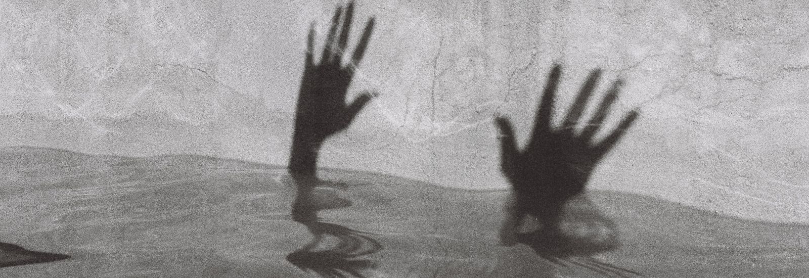 Black and white image shows pool of water with shadow on wall behind of two hands reaching out of it