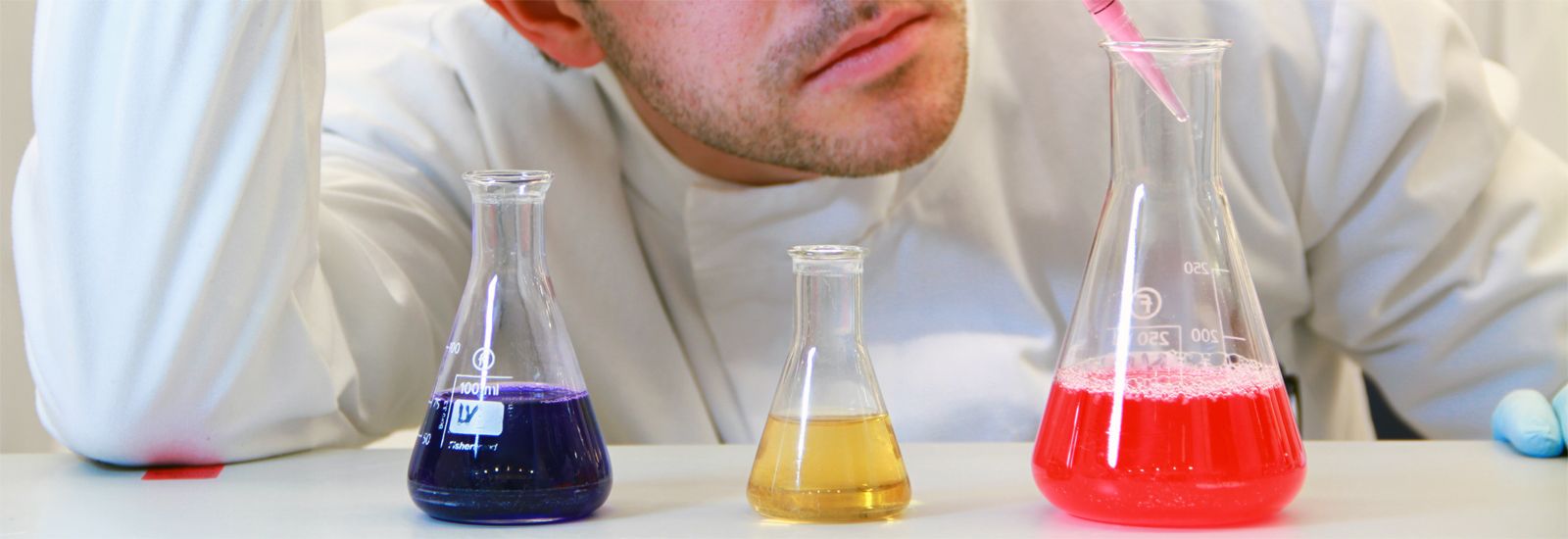 Student with 3 test tubes with coloured liquids 