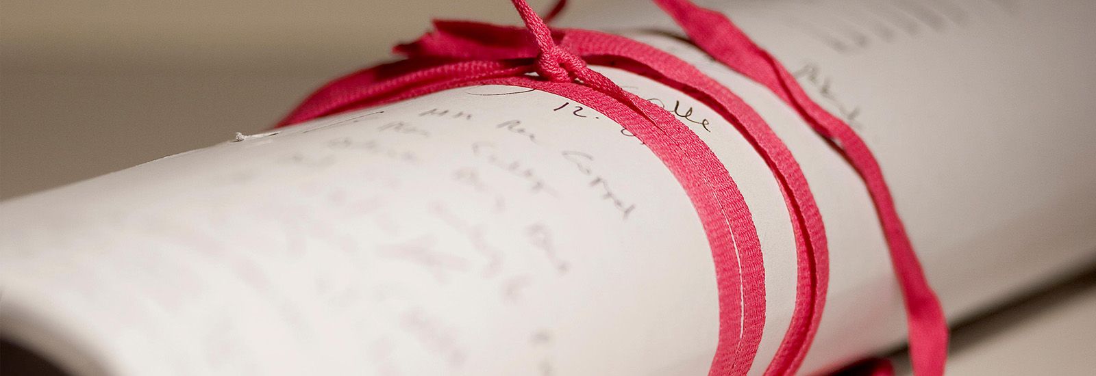 Close up of a handwritten document rolled and tied with a red ribbon