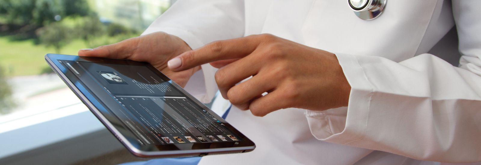 A medical professional wearing a white coat and stethoscope uses communications software on a portable tablet 