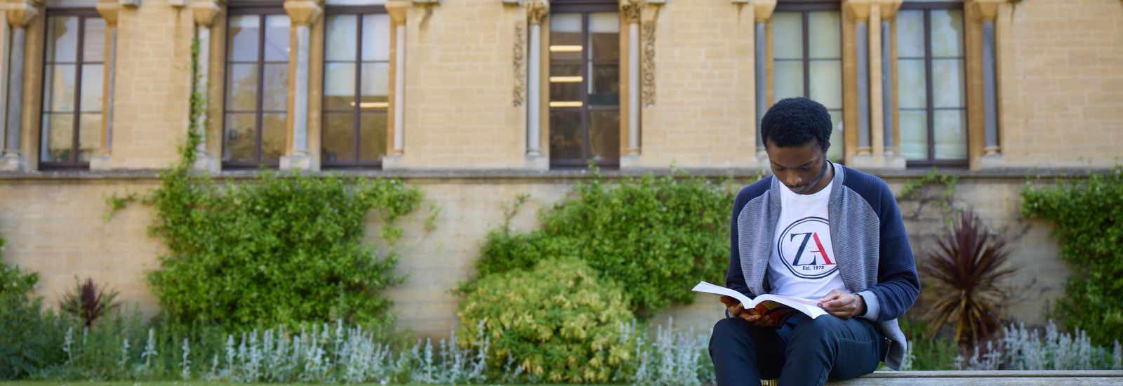 Student sat reading in front of the Museum of Natural History, Oxford.