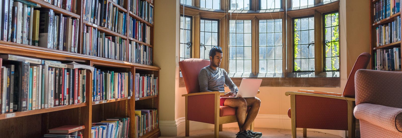 Student sitting with a laptop in the bay window of a library 