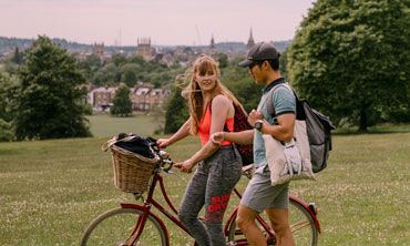 Two students walk across a park, with Oxford's skyline in the background