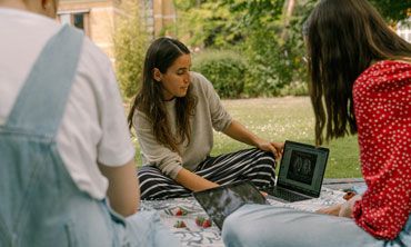 A student showing her laptop to friends, as they work outside