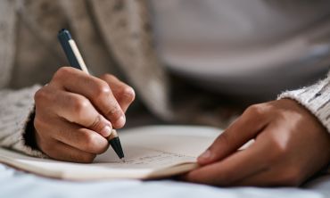 A close-up image of someone's hands, writing in a notebook with a pen
