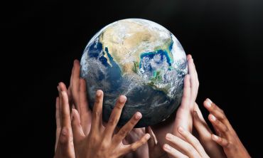 Image of multiple diverse hands reaching for and holding up planet Earth