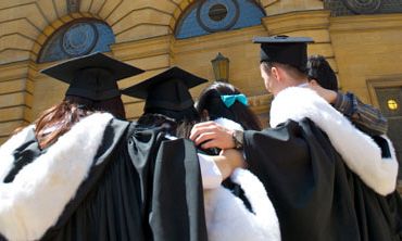 Four students in Oxford University graduation gowns with their arms around each other