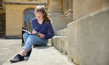 Student sat on steps with a notebook. Ian Wallman Photography