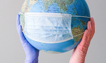 Hands with latex gloves holding a globe with a face mask. 