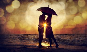 Generic image of couple kissing under umbrella at the beach in sunset. 