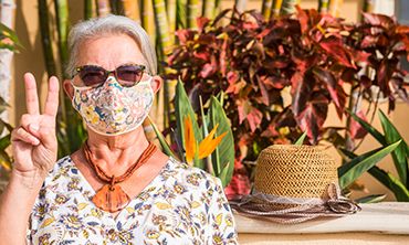 Senior woman wearing floral mask due to coronavirus making peace sign