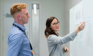 A woman drawing on a whiteboard, explaining something to a man