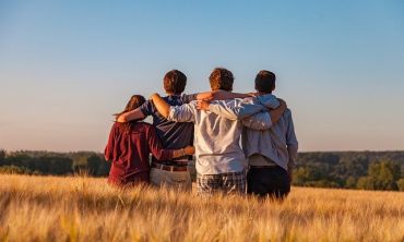 Group of young people standing back in a field and holding each other around their shoulders. 