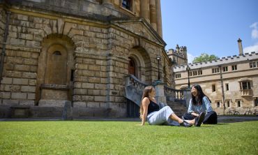 Two students sitting on the grass outside the Radcliffe Camera on a sunny day.