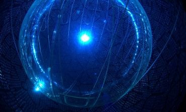 A round chamber with walls made up of photomultiplier tubes, illuminated by a central blue light.