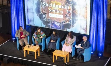 Aerial view of stage with panellists and moderator in discussion with Sheldonian Series graphic on a screen behind them
