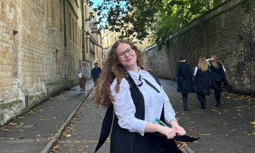 Daphne Harries stands, smiling, in sub fusc in Brasenose Lane