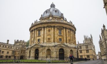 Landscape photo of the Radcliffe Camera and surrounding buildings with a cyclist in the foreground