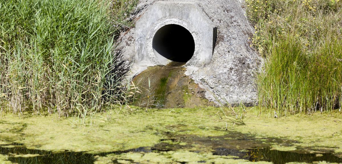 A wastewater pipe in a river bank dishcharges a stream of dirty water into a river. 