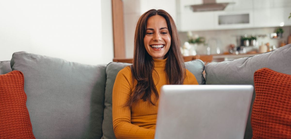 Young woman smiles at laptop while sitting on sofa