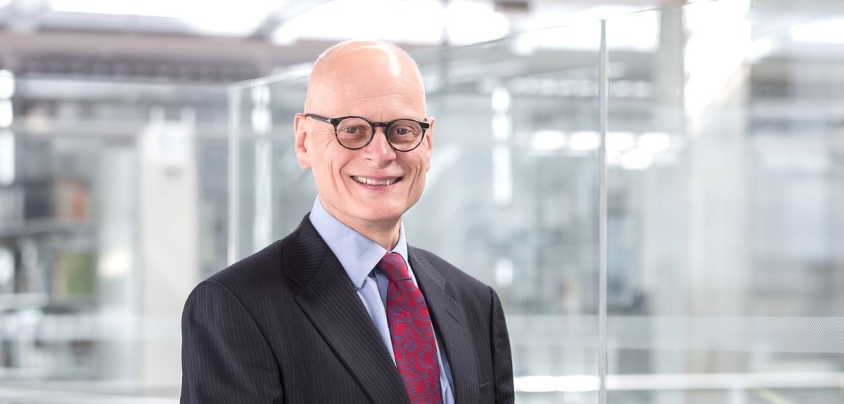 A bald white man wearing glasses, a smart jacket and a tie.