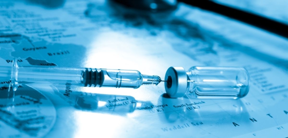 Image depicting a vaccine syringe and vial resting on top of a map