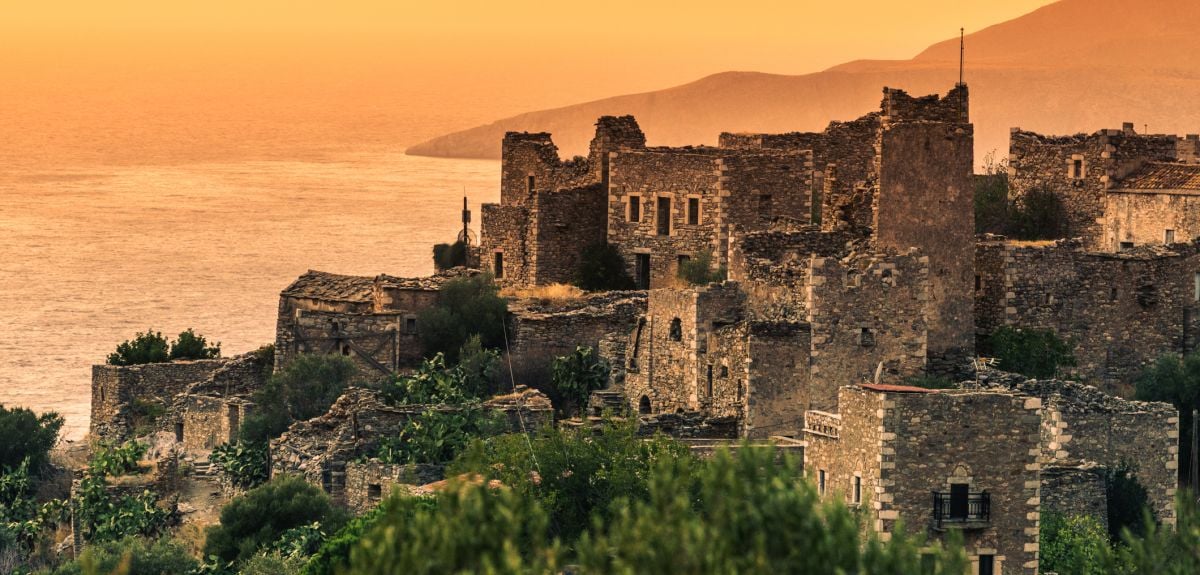 Old abandoned tower houses in Vathia Mani Peninsula at evening time, with the sun setting over the ocean. 
