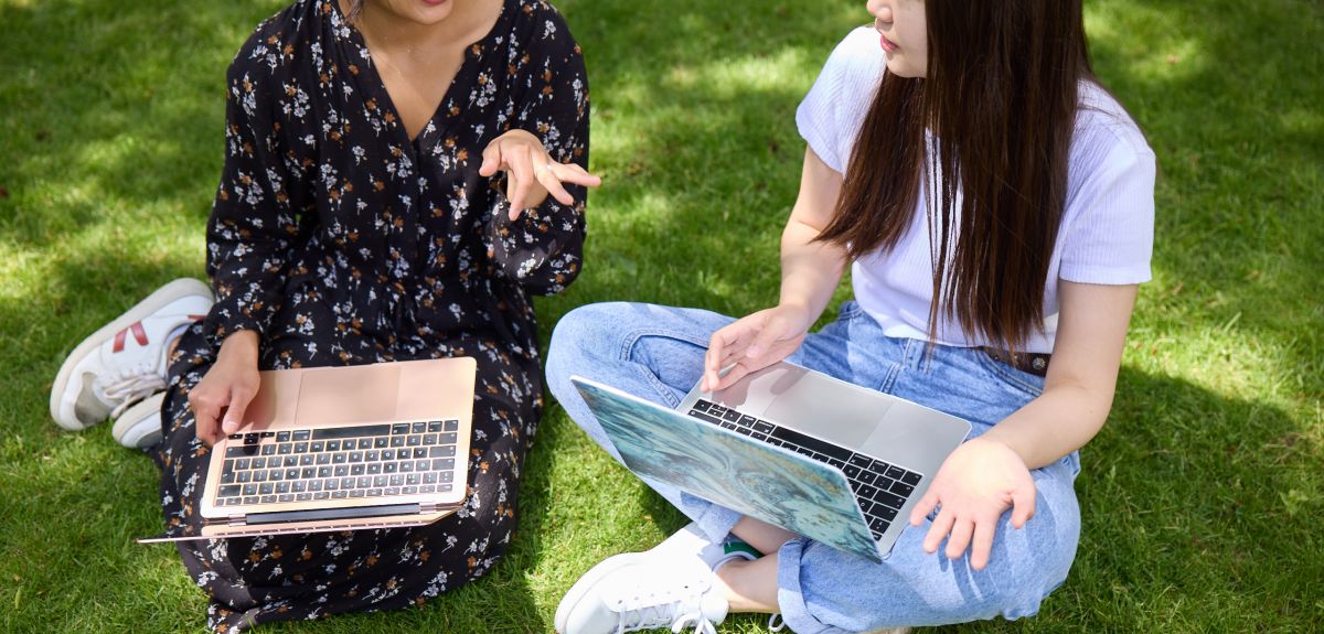 Two people sat on grass with their laptops. 