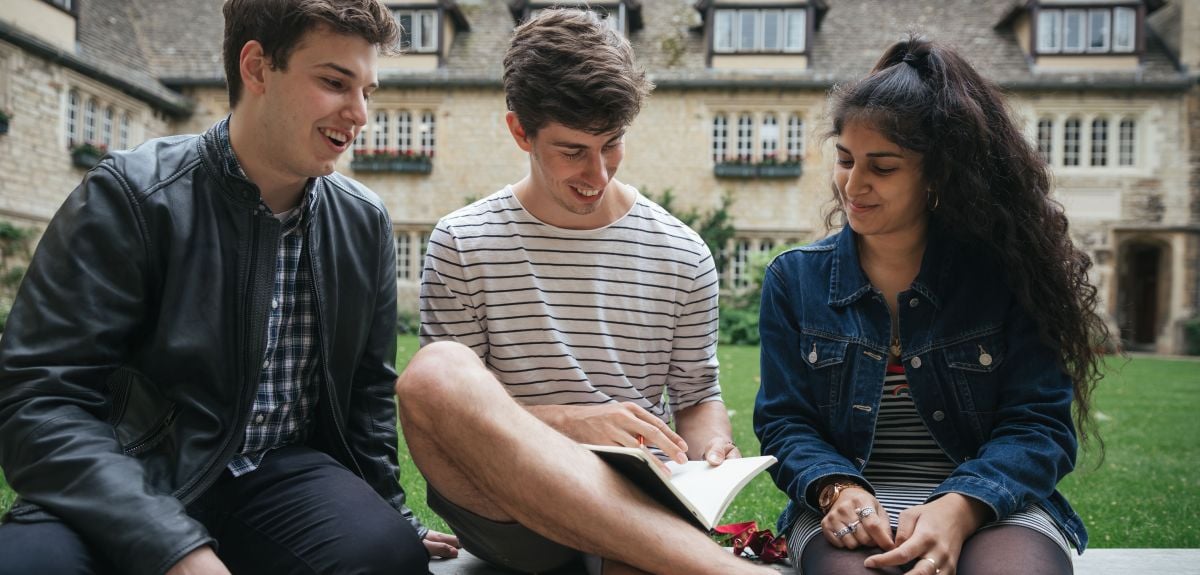 Three students sitting on a bench in a college garden.