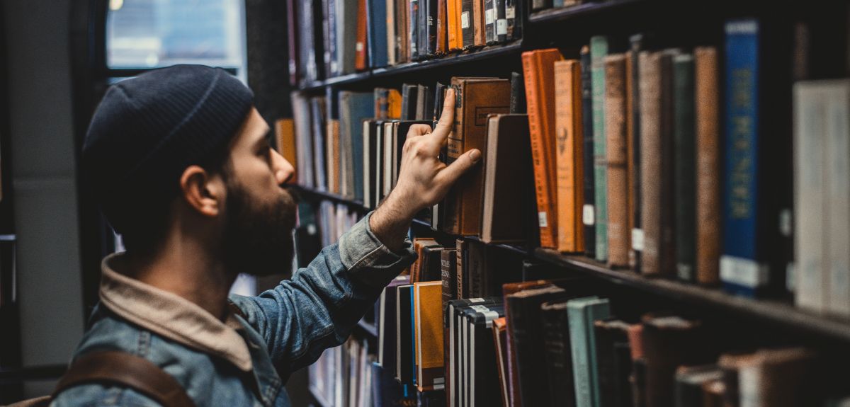  Man selecting a book from a library bookshelf. Photo by Devon Divine on Unsplash 